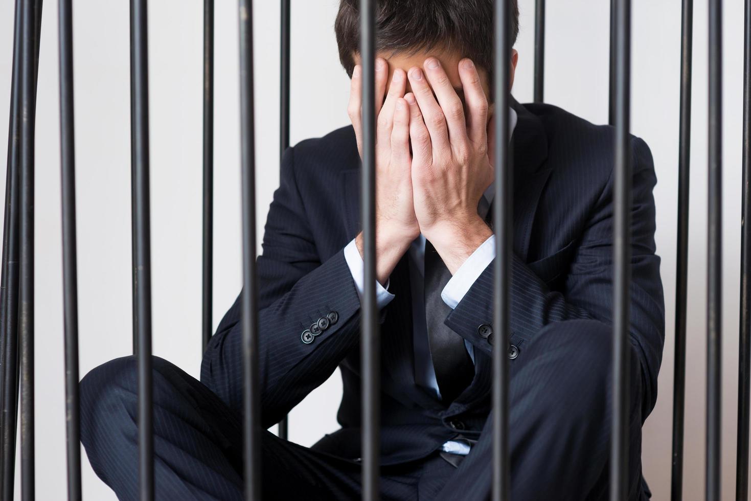 criminel d'affaires. jeune homme déprimé en tenues de soirée debout derrière une cellule de prison et regardant loin photo