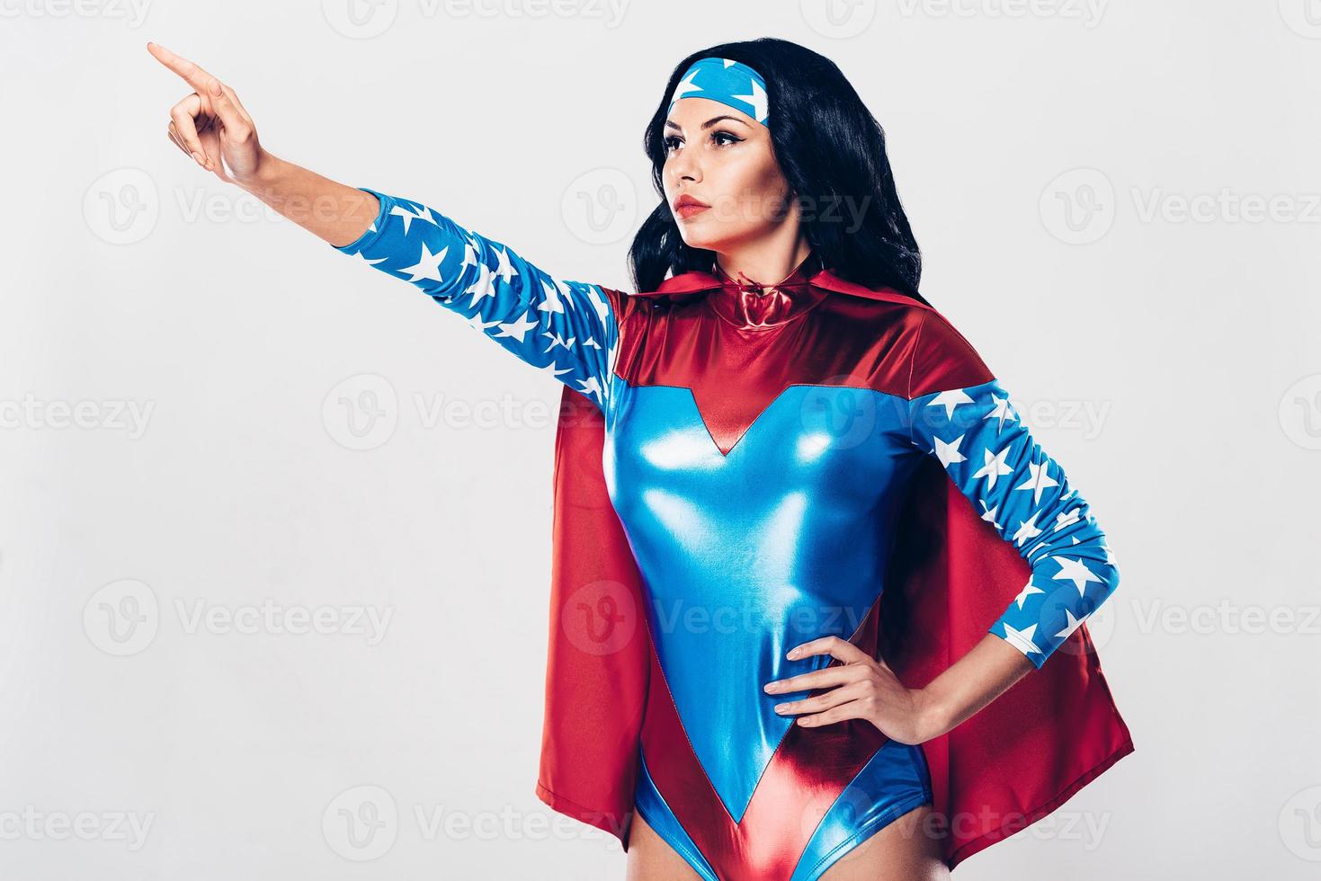 elle sait où la justice est nécessaire. vue latérale d'une belle jeune femme en costume de super-héros pointant vers l'extérieur en se tenant debout sur fond blanc photo