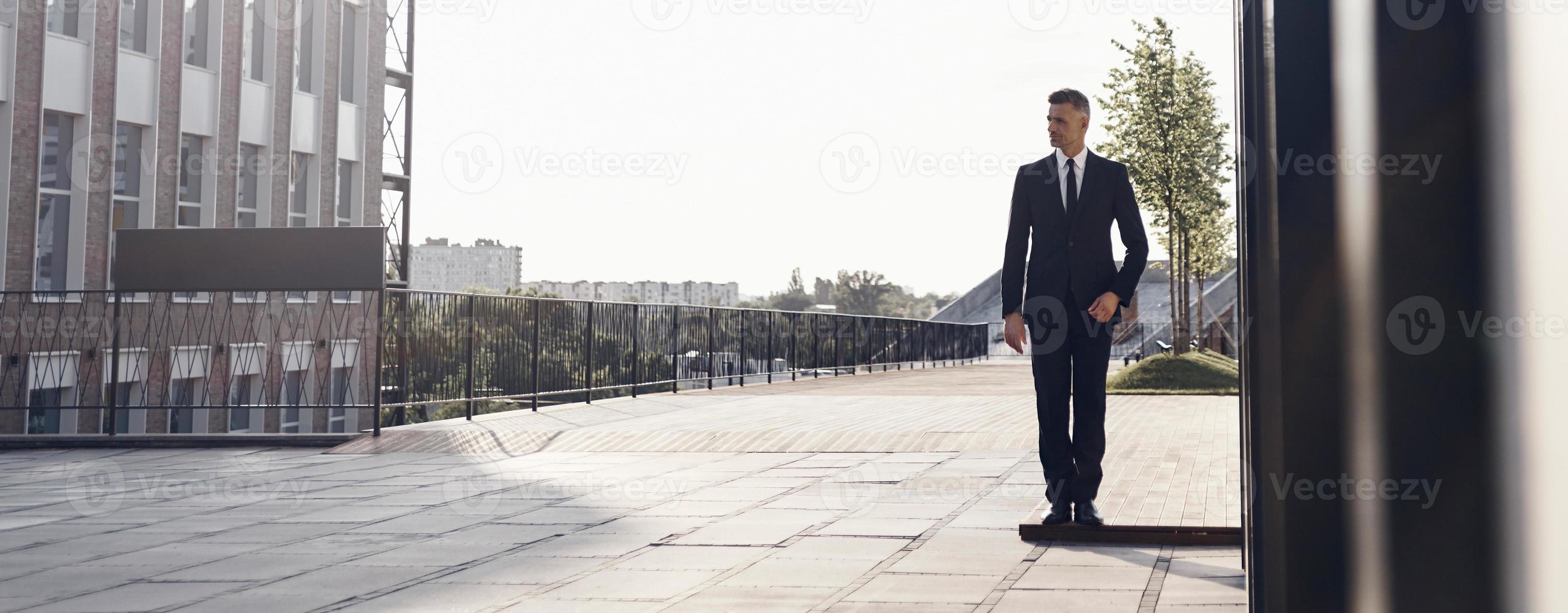 homme d'affaires mature confiant marchant près d'un immeuble de bureaux à l'extérieur photo