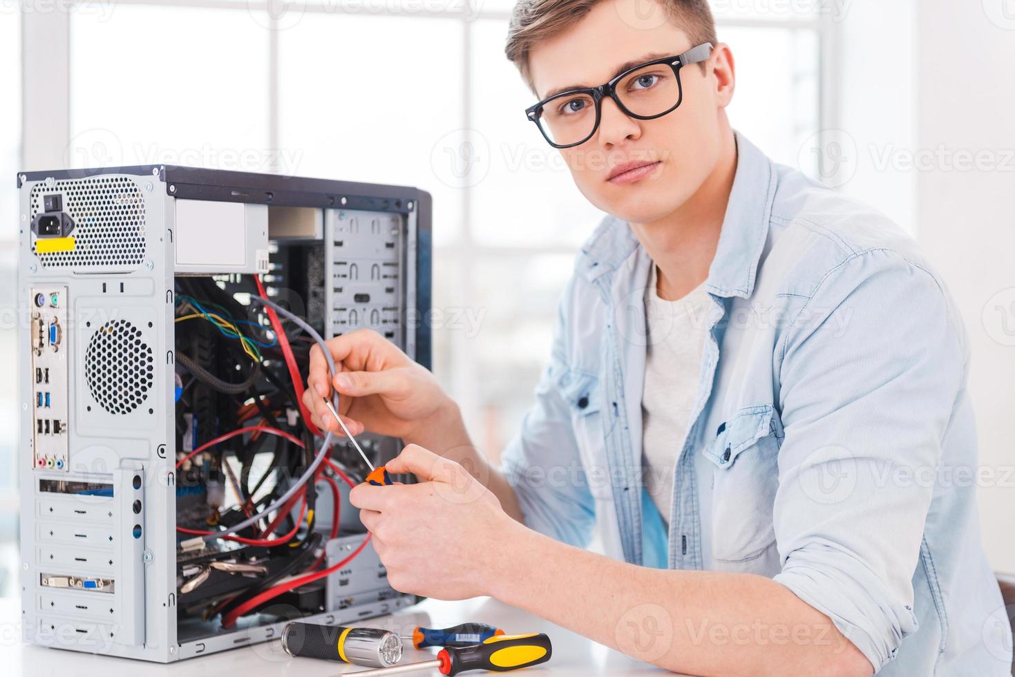 professionnel intelligent. portrait d'un beau jeune homme réparant un ordinateur assis sur son lieu de travail photo