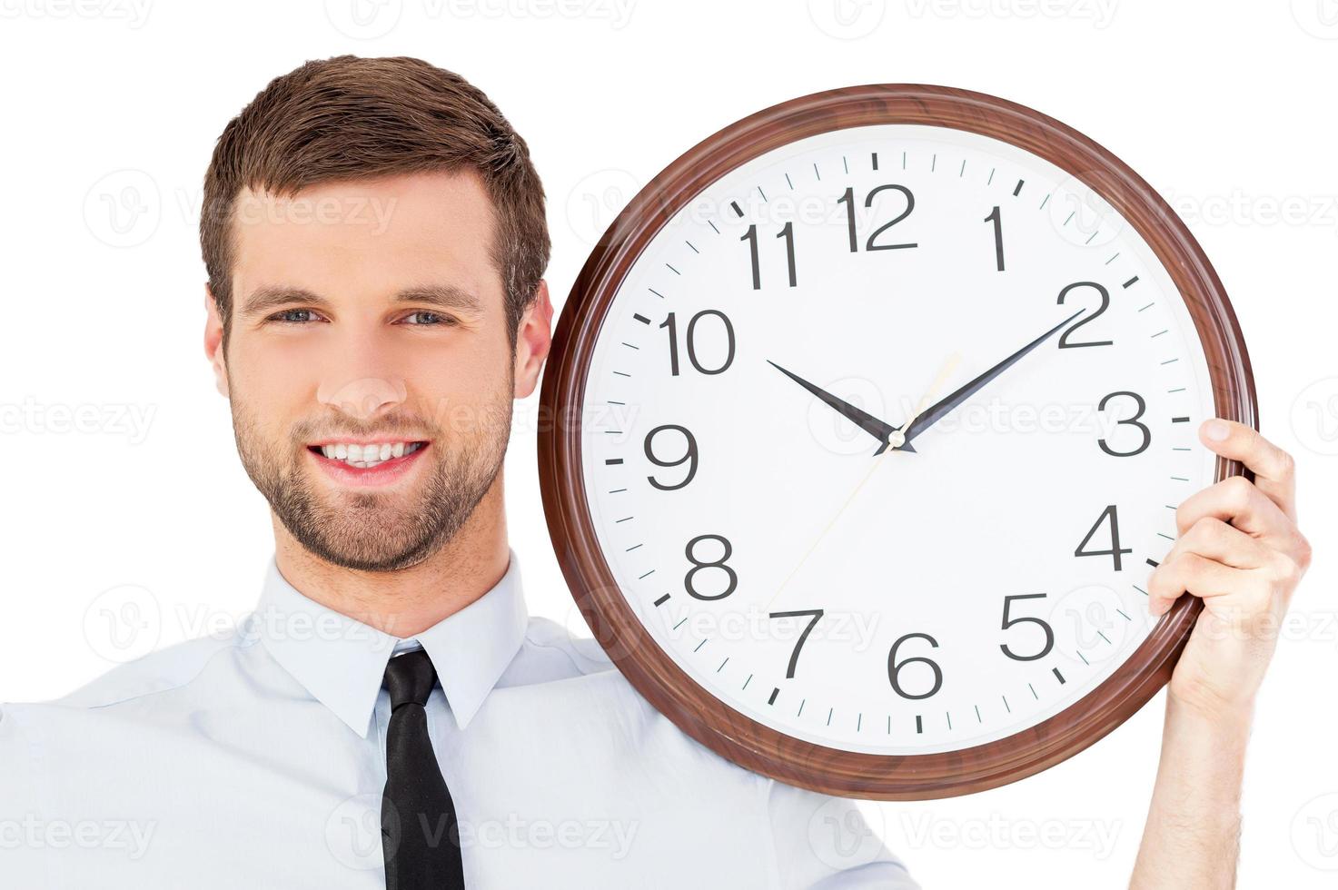 prenez votre temps beau jeune homme en tenues de soirée tenant une horloge sur son épaule et souriant debout isolé sur fond blanc photo