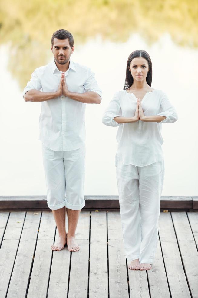 trouver la paix ensemble. toute la longueur du beau jeune couple en vêtements blancs méditant ensemble à l'extérieur photo