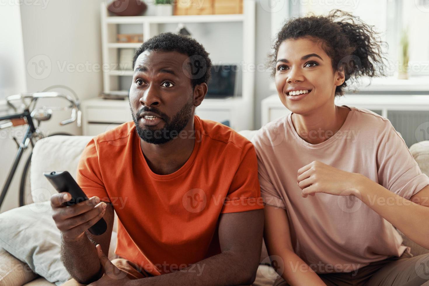beau jeune couple africain regardant la télévision et souriant tout en passant du temps à la maison photo