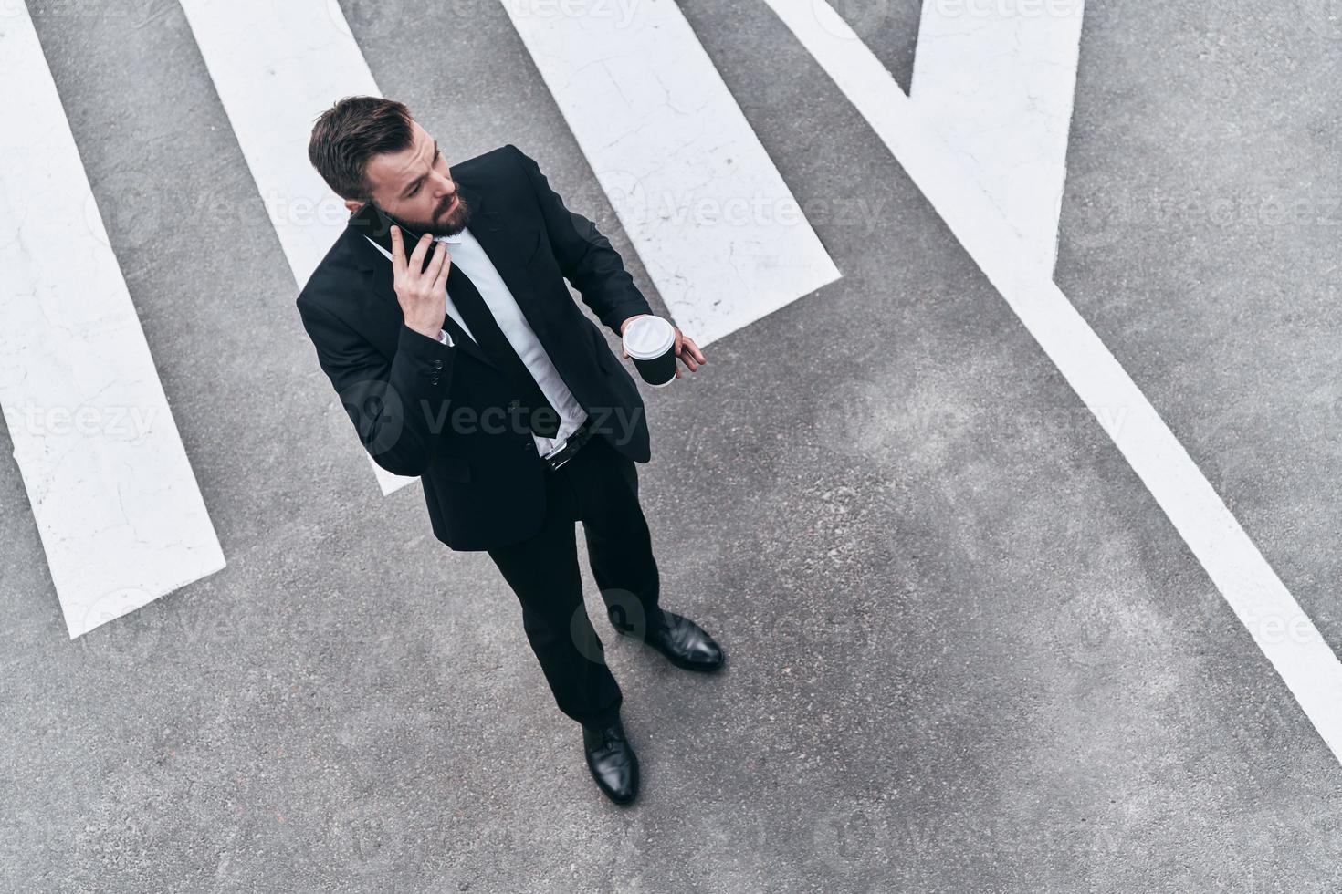 s'occuper des affaires. vue de dessus pleine longueur d'un jeune homme en costume complet parlant au téléphone tout en se tenant à l'extérieur photo