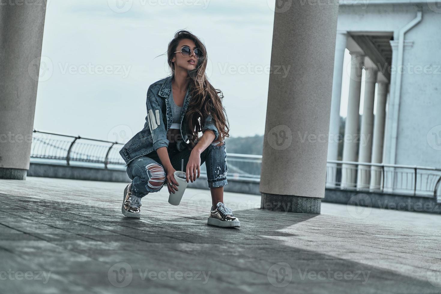 elle est tout au sujet de la mode. belle jeune femme en jeans porter à la recherche de suite et tenant une tasse jetable tout en passant du temps à l'extérieur photo