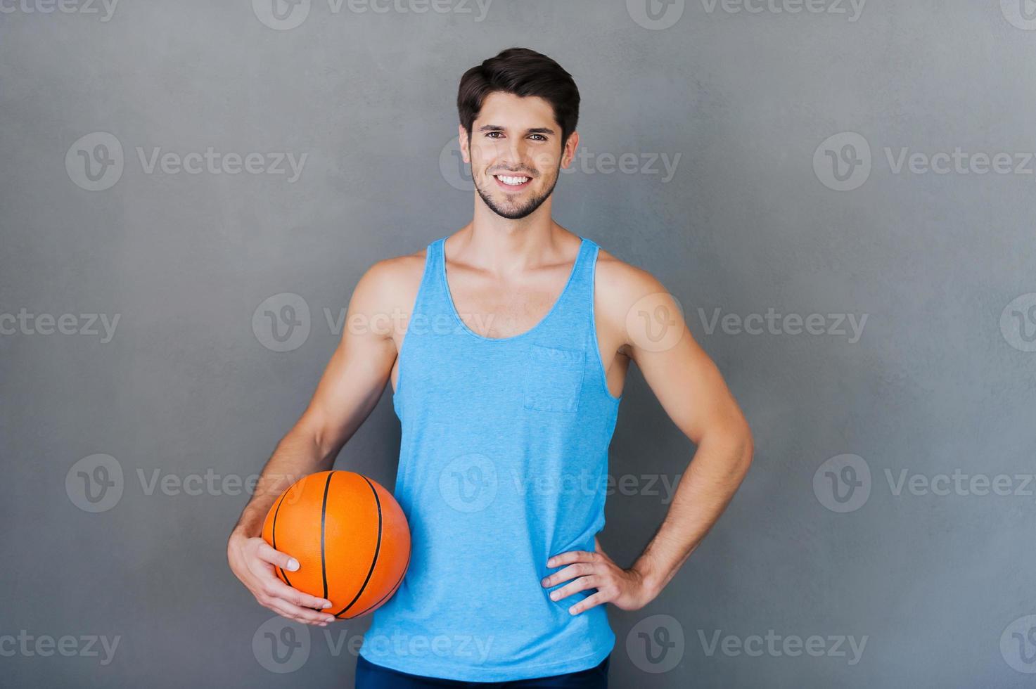 êtes-vous prêt pour le jeu heureux jeune homme musclé tenant un ballon de basket en se tenant debout sur fond gris photo