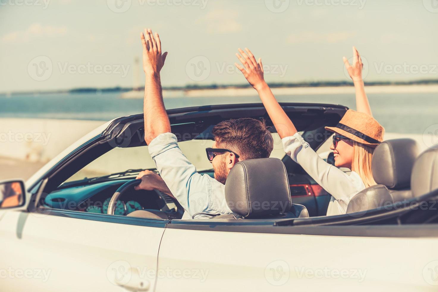 parfait début de leur week-end. jeune couple excité gardant les bras levés tout en roulant dans leur cabriolet blanc photo