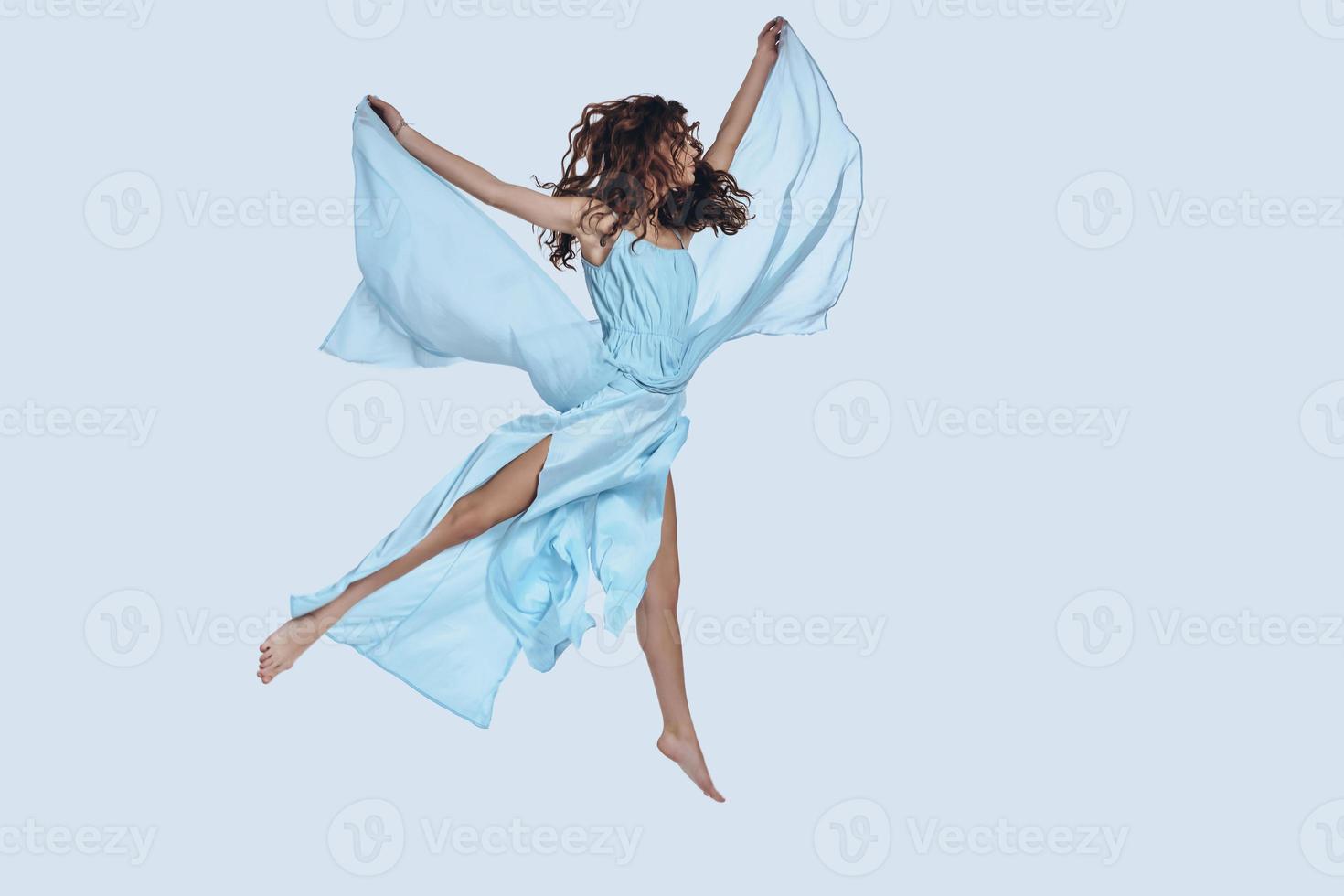 en volant. prise de vue en studio pleine longueur d'une jeune femme séduisante en robe élégante gardant les bras tendus tout en planant sur fond gris photo