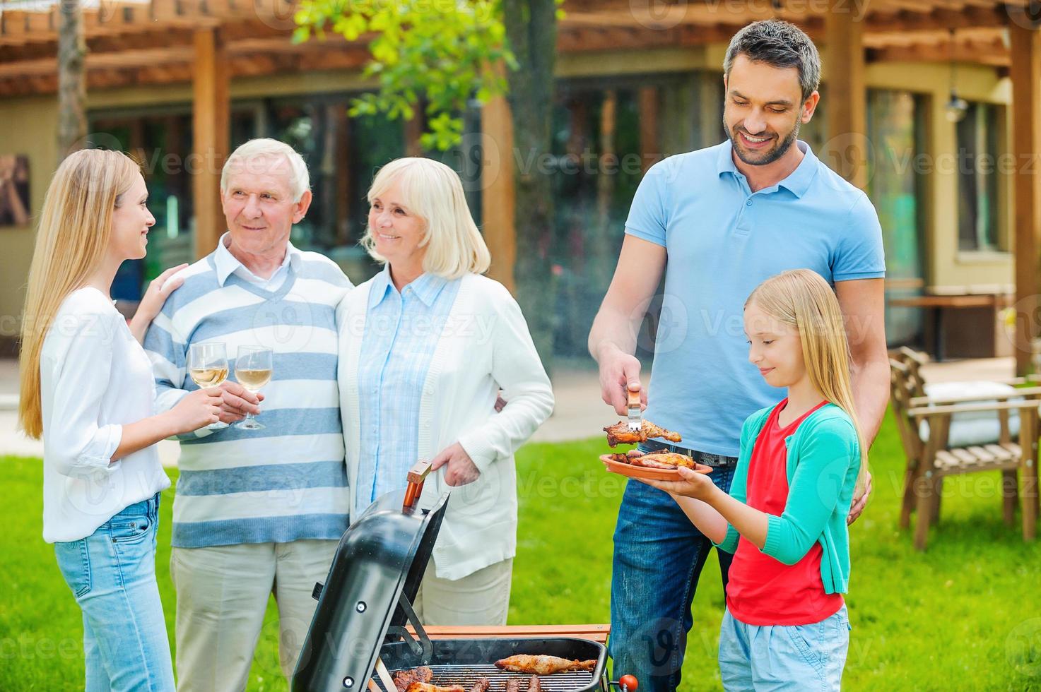 passer de bons moments en famille. famille heureuse de cinq personnes faisant griller de la viande sur le gril dans la cour arrière photo