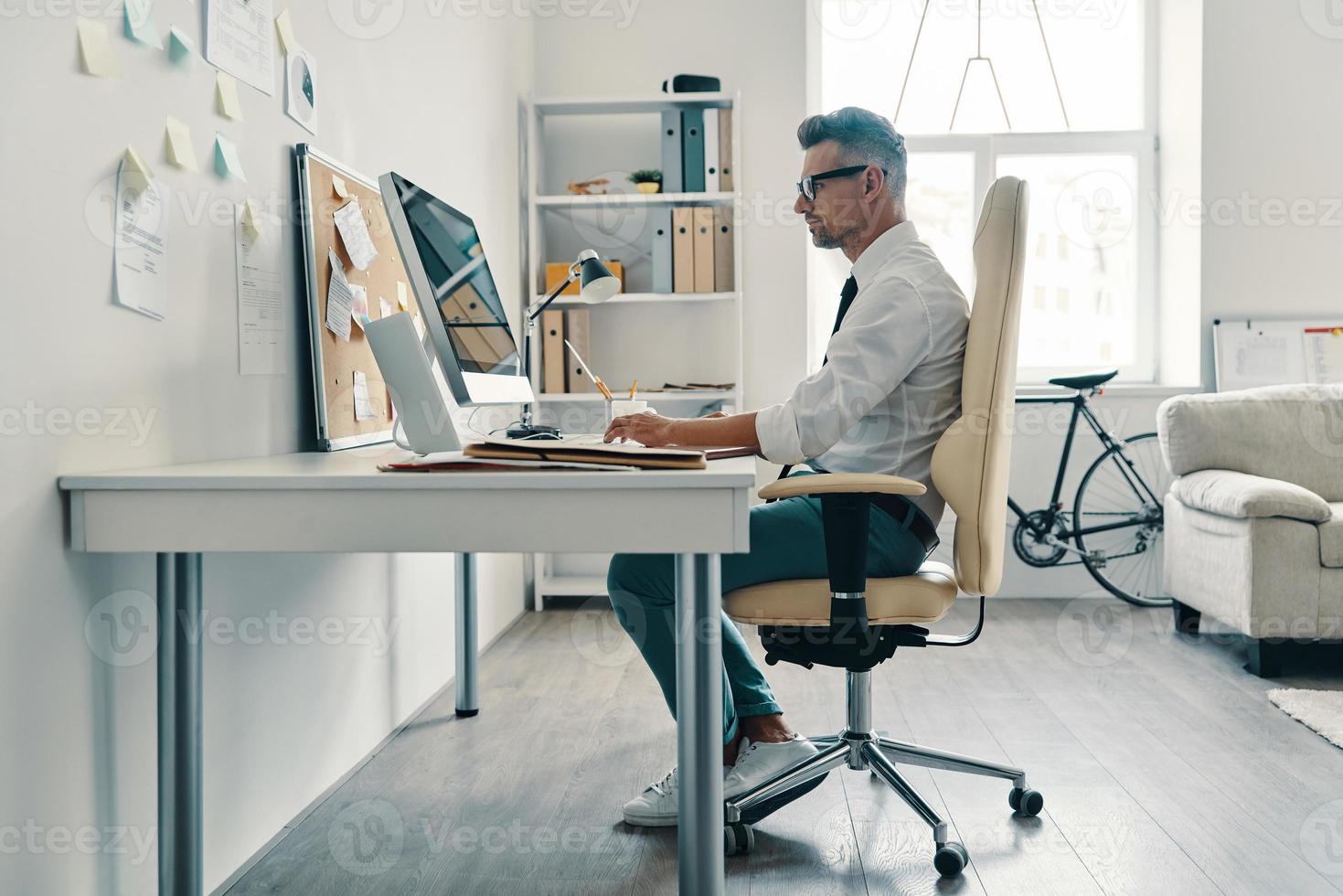 les affaires sont sa vie. jeune homme réfléchi en chemise et cravate travaillant à l'aide d'un ordinateur assis au bureau photo