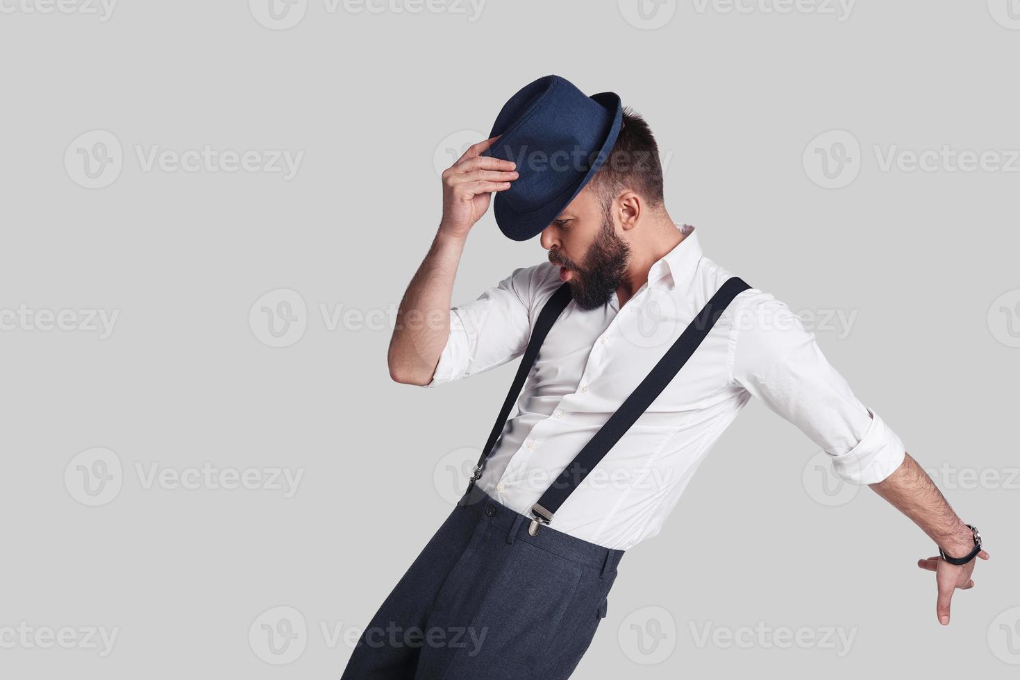 il a obtenu les mouvements. beau jeune homme en bretelles ajustant son chapeau et faisant une grimace en dansant sur fond gris photo