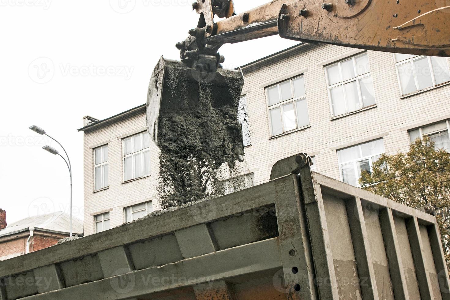 travaux routiers dans la rue de la ville. le godet de la pelle récupère l'ancien revêtement et le charge dans un camion à benne basculante photo