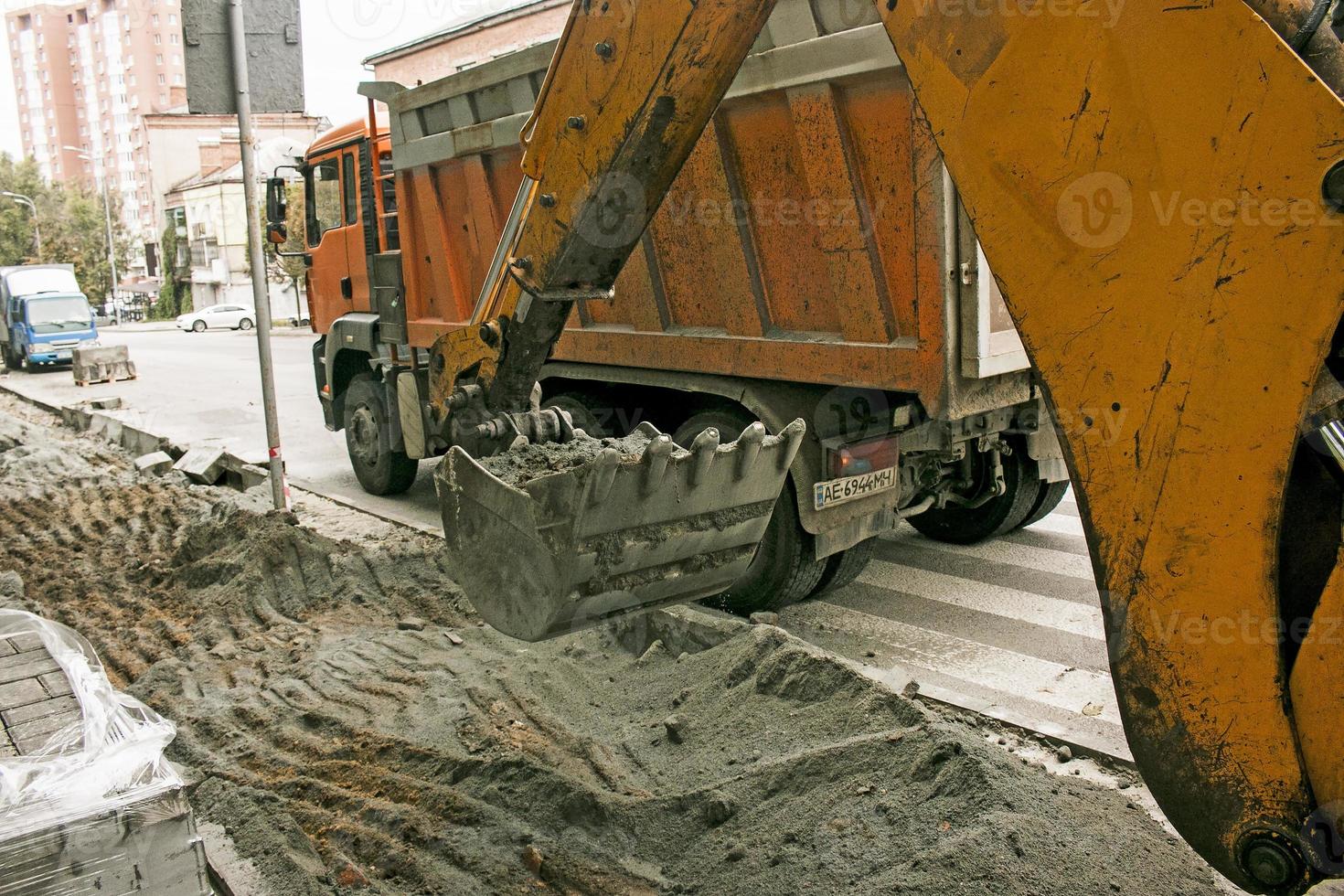 travaux routiers dans la rue de la ville. le godet de l'excavatrice récupère l'ancien revêtement et le charge dans un camion à benne basculante. photo