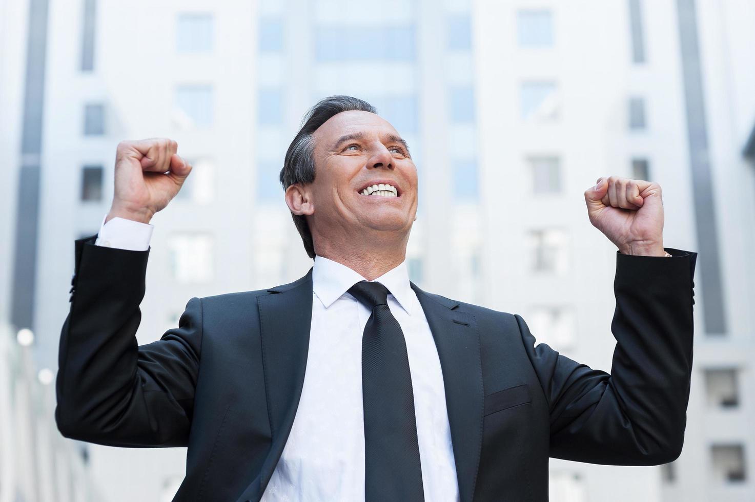 gagnant de tous les jours. heureux homme âgé en tenue de soirée gardant les bras levés et exprimant sa positivité tout en se tenant à l'extérieur photo