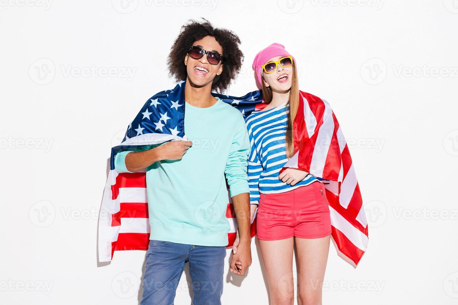 insouciant et amoureux. funky jeune couple couvrant de drapeau américain et souriant en se tenant debout sur fond blanc photo