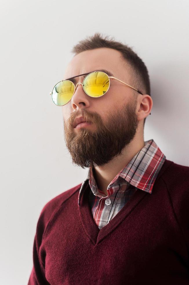 à la mode. beau jeune homme à lunettes de soleil appuyé contre le mur et regardant au loin photo