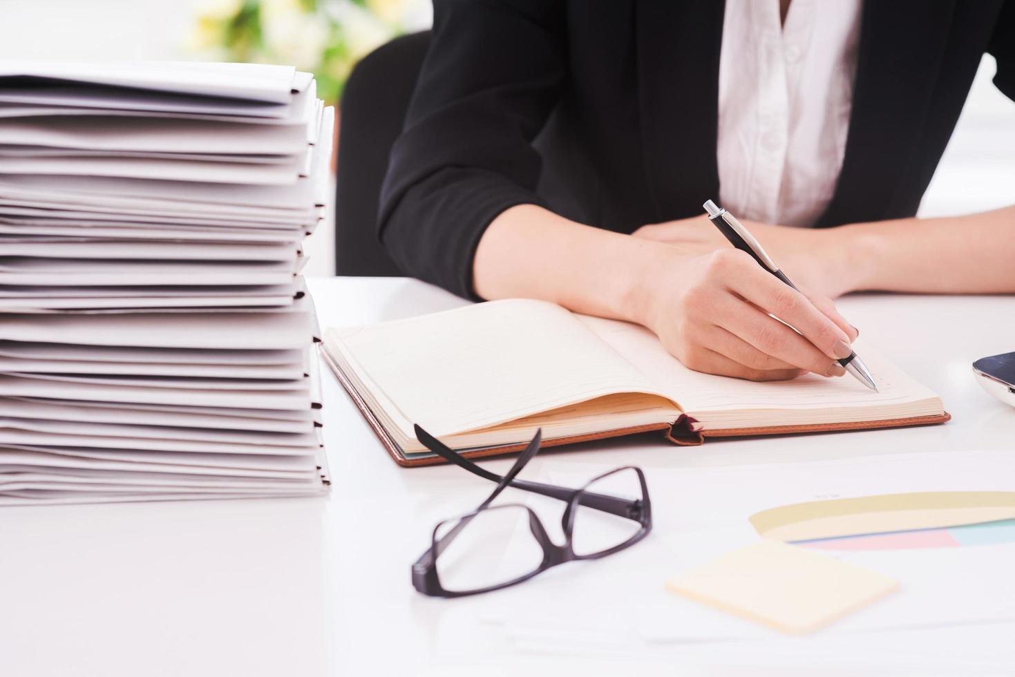 faire du travail de bureau. image recadrée d'une femme écrivant des notes assise sur son lieu de travail photo