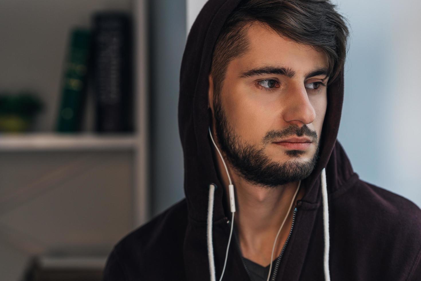 se sentir triste. portrait d'un jeune homme pensif en chemise à capuche regardant loin tout en se tenant à la maison photo