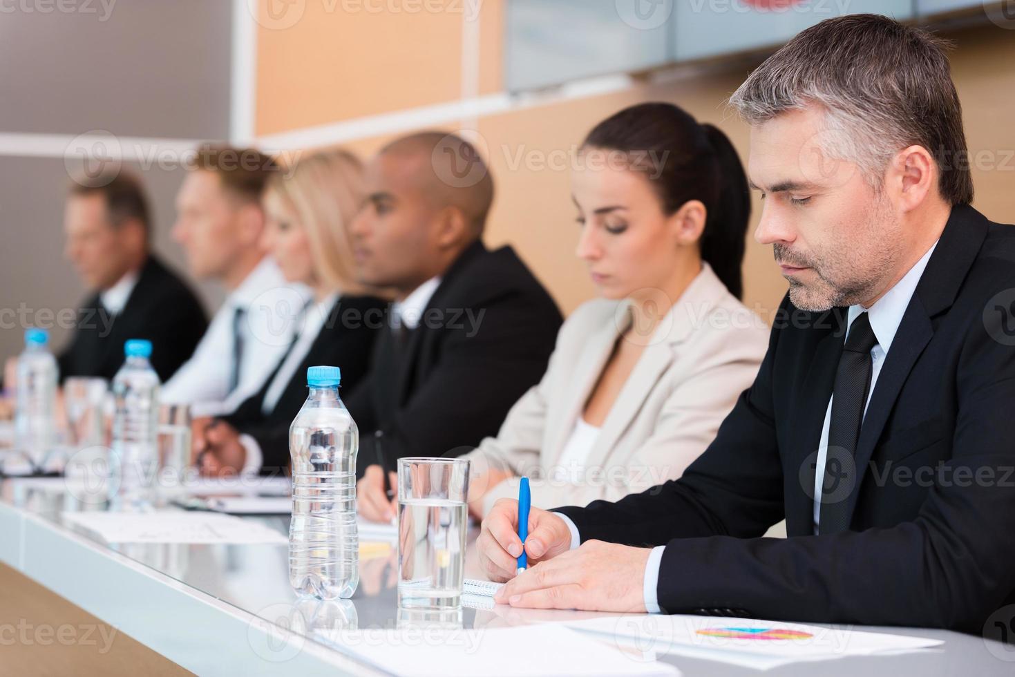 conférence d'affaires. vue latérale d'hommes d'affaires écrivant quelque chose dans leurs blocs-notes assis dans une rangée photo