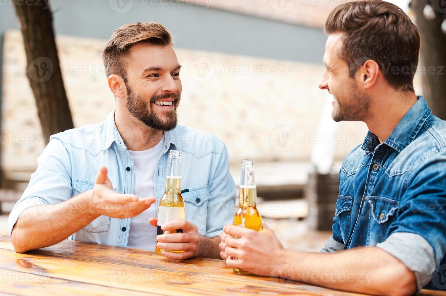 bonne conversation avec un ami. deux jeunes hommes joyeux se parlent et tiennent des bouteilles de bière tout en se tenant à l'extérieur photo