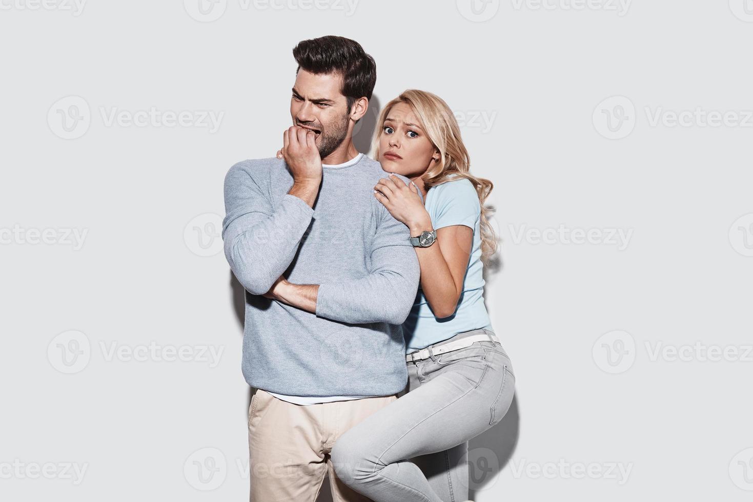 craindre. jeune couple terrifié faisant une grimace en se tenant debout sur fond gris photo