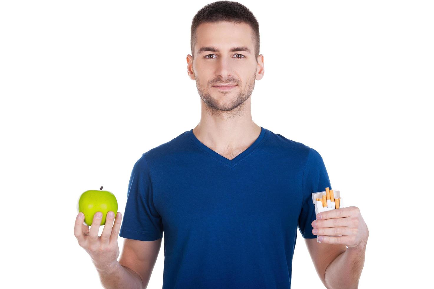 faire le bon choix. jeune homme confiant tenant une pomme dans une main et un paquet de cigarettes dans une autre et isolé sur blanc photo