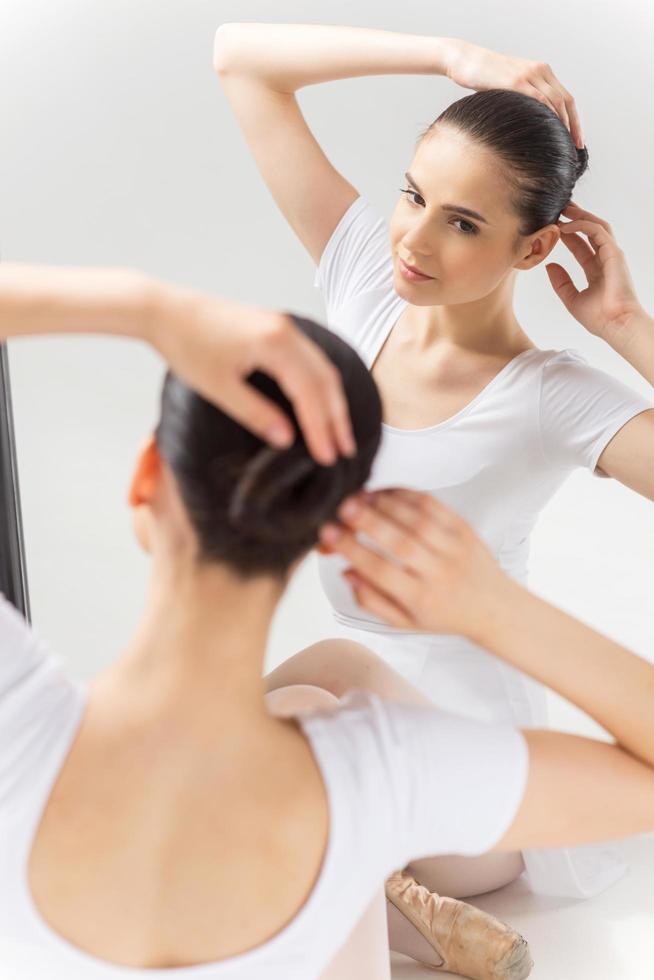 en s'assurant qu'elle a l'air parfaite. jeune ballerine confiante ajustant ses cheveux assise contre un miroir et regardant son reflet photo