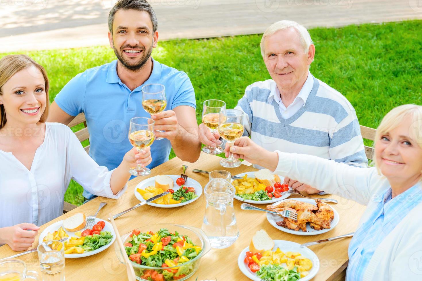 grillage familial avec du vin. vue de dessus d'une famille heureuse assise à la table à manger et portant un toast avec du vin photo