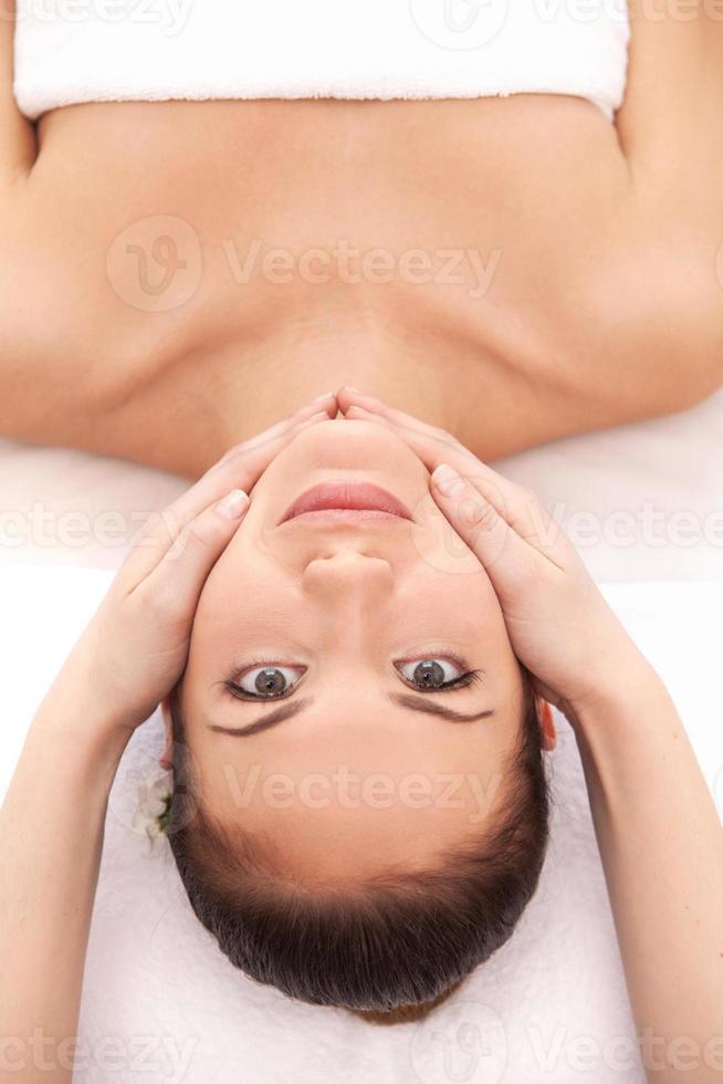 profiter d'un massage du visage. vue de dessus d'une jeune femme joyeuse allongée sur le dos et regardant la caméra pendant que le massothérapeute lui masse le visage photo