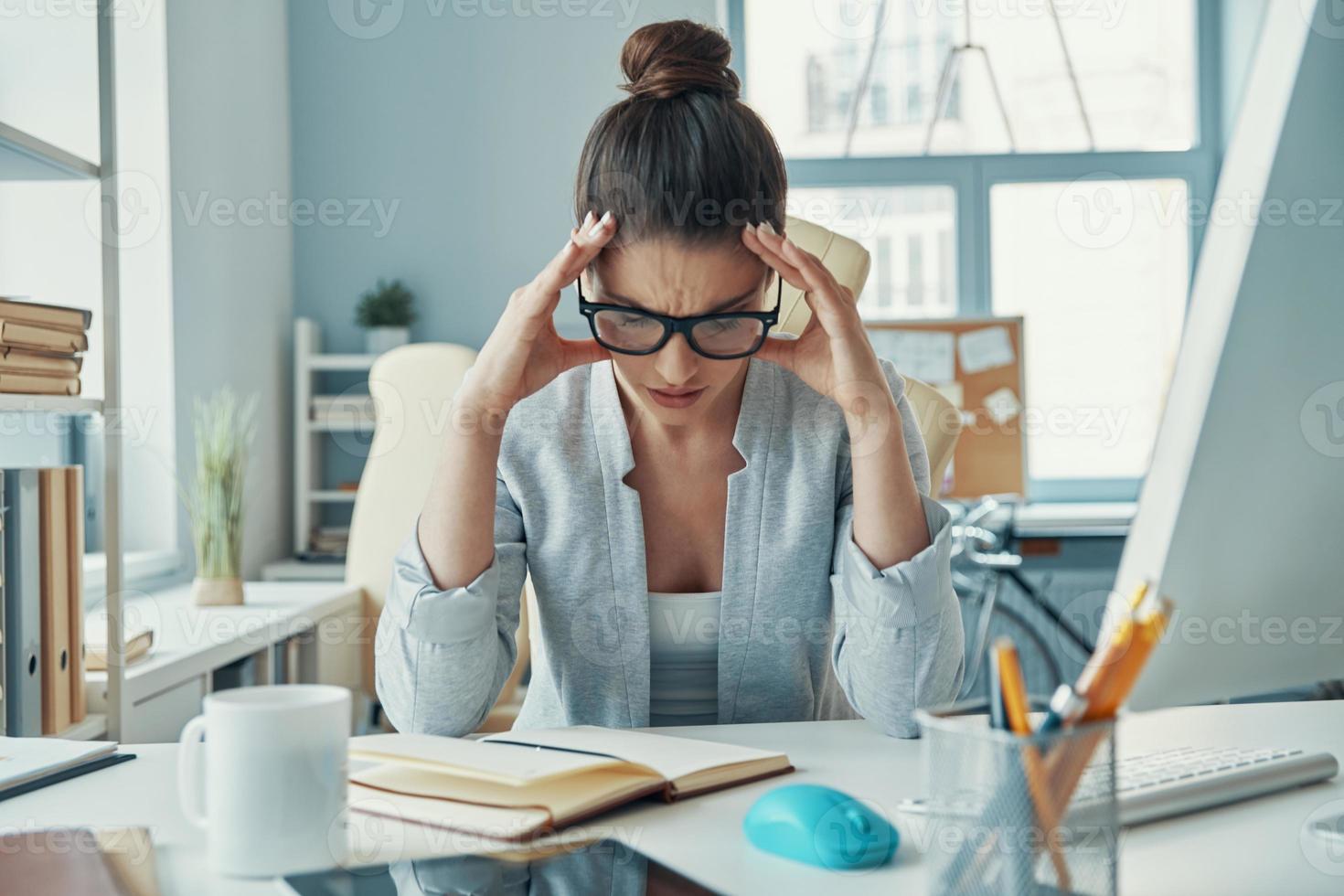 jeune femme stressée en tenue décontractée intelligente gardant la tête dans les mains tout en étant assise au bureau photo