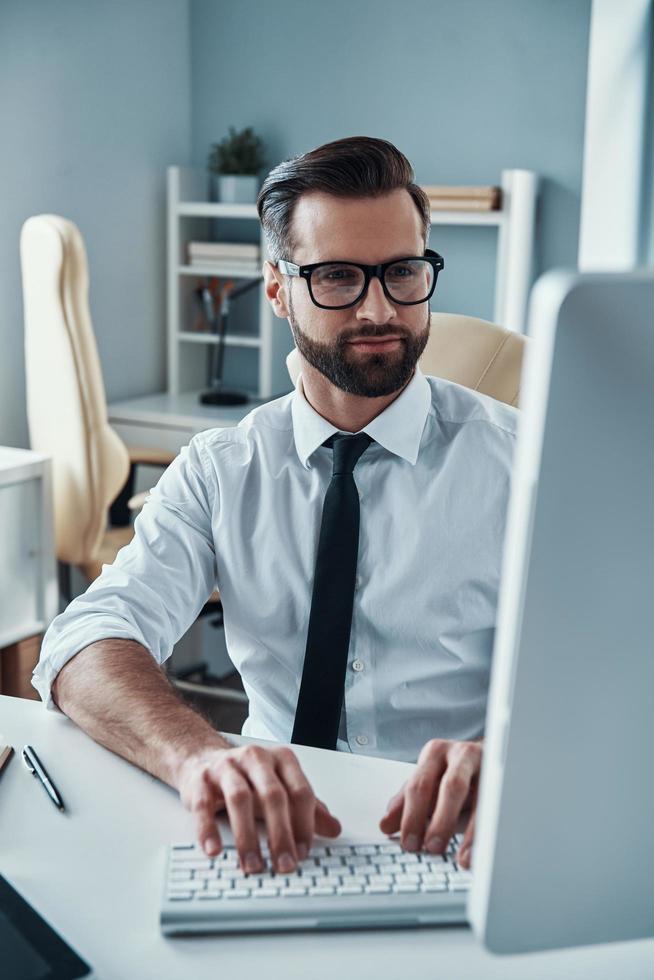 jeune homme moderne en tenue de soirée travaillant sur ordinateur assis au bureau photo