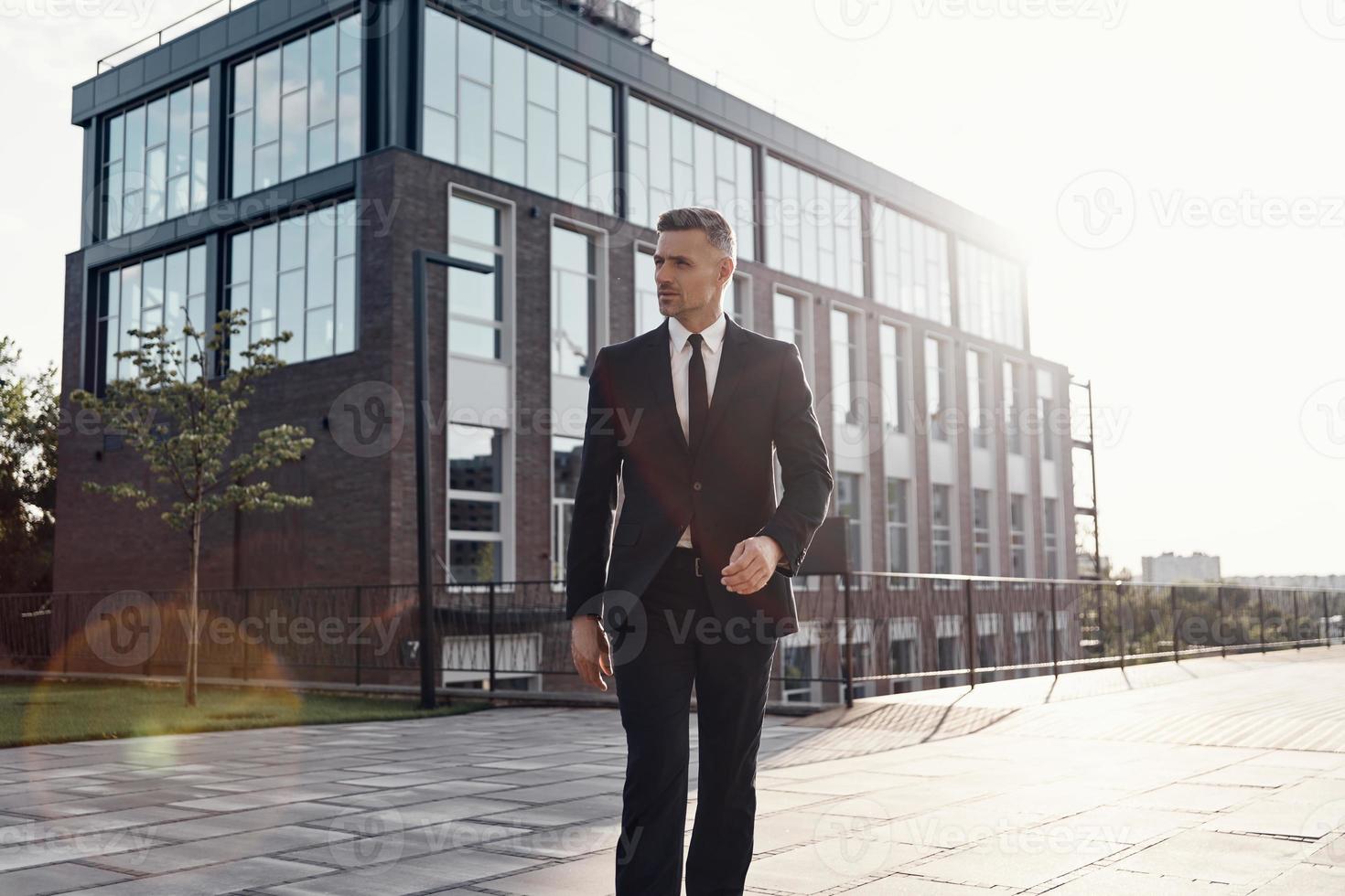 homme d'affaires mature confiant marchant près d'un immeuble de bureaux à l'extérieur photo