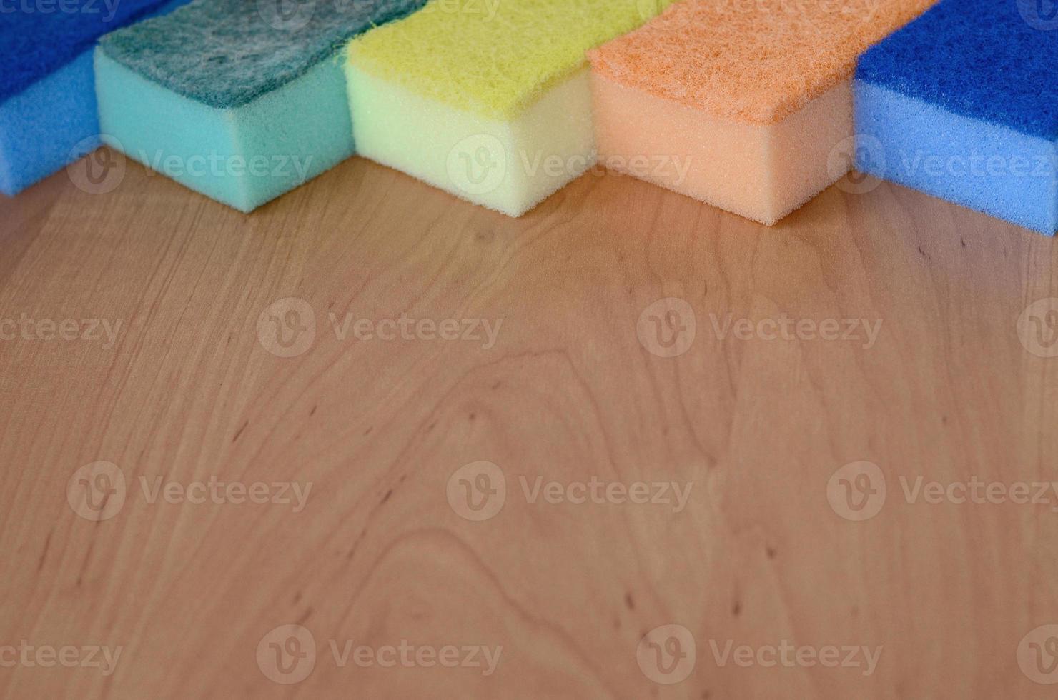 quelques éponges de cuisine reposent sur un comptoir de cuisine en bois. des objets colorés pour laver la vaisselle et nettoyer dans la maison sont prêts à l'emploi photo