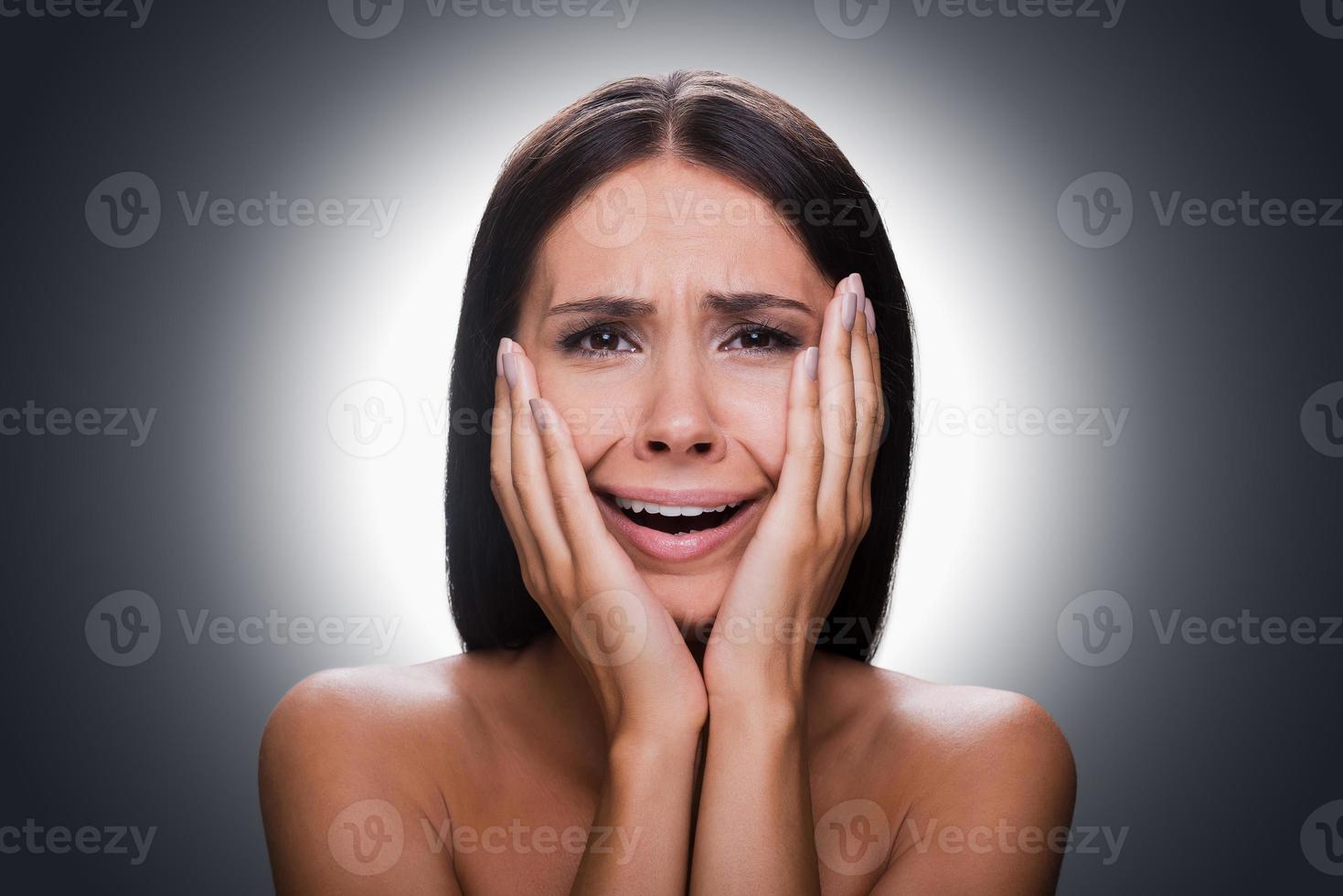 un sentiment de désespoir. portrait de jeune femme torse nu frustrée touchant la tête avec les mains et regardant la caméra en se tenant debout sur fond gris photo