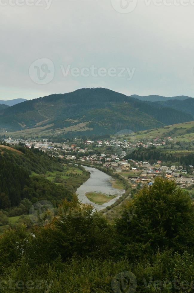 une belle vue sur le village de mezhgorye, région des carpates. beaucoup de bâtiments résidentiels entourés de hautes montagnes forestières et d'une longue rivière photo