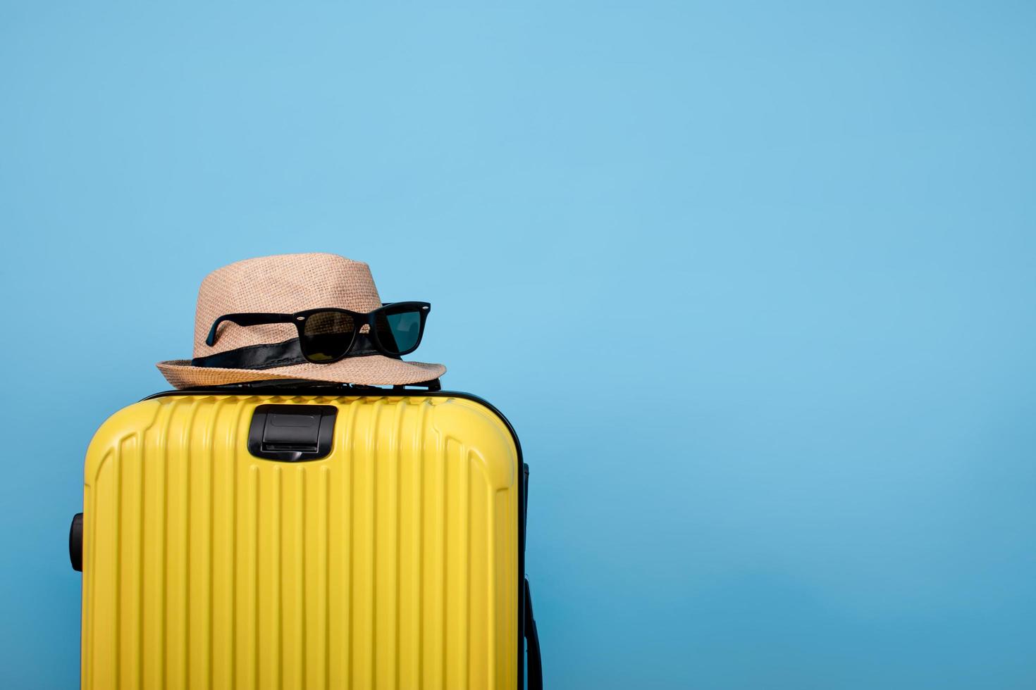 Libre de valise jaune avec chapeau et lunettes de soleil sur fond bleu photo