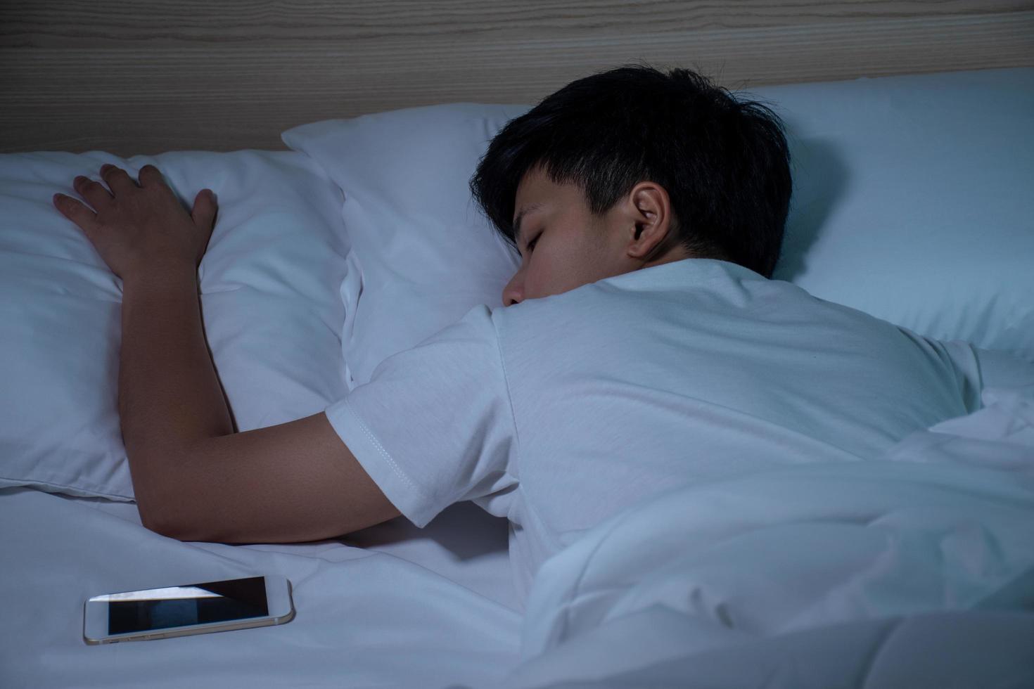 les asiatiques dorment dans un lit avec un smartphone. photo