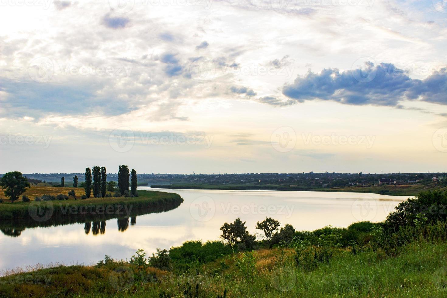 soirée d'été aube ciel nuages réfléchis sur un lac d'eau sur la côte avec de l'herbe verte et des arbres forestiers photo