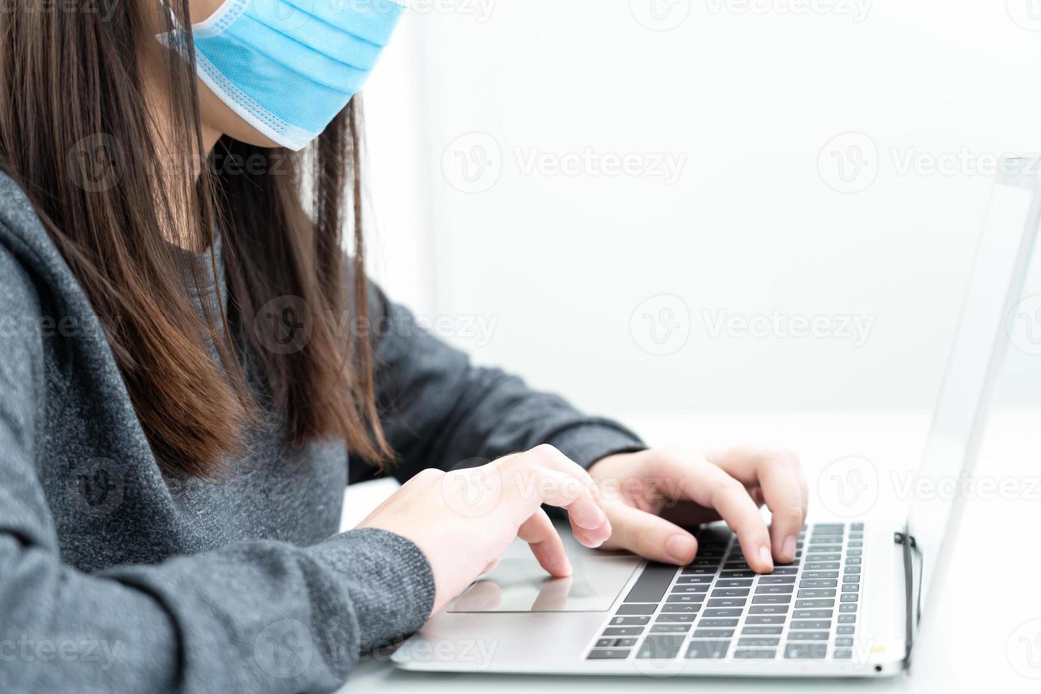 femme utilisant un ordinateur portable sur le bureau à la maison avec un masque pour protéger covid-19 photo