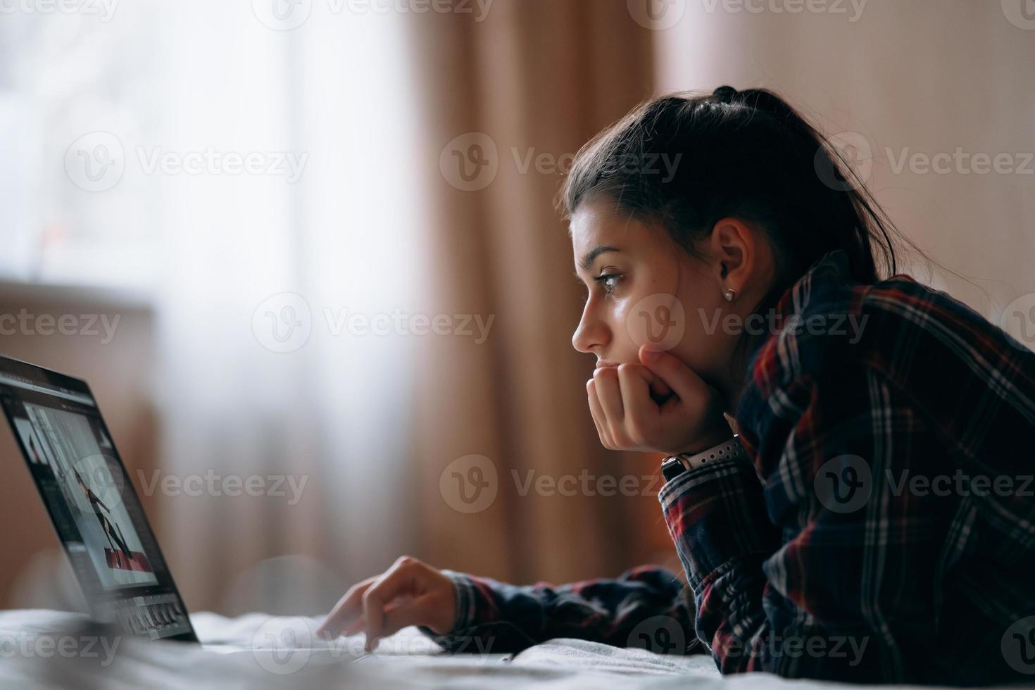 jeune femme travaille avec un ordinateur portable allongé sur le lit photo