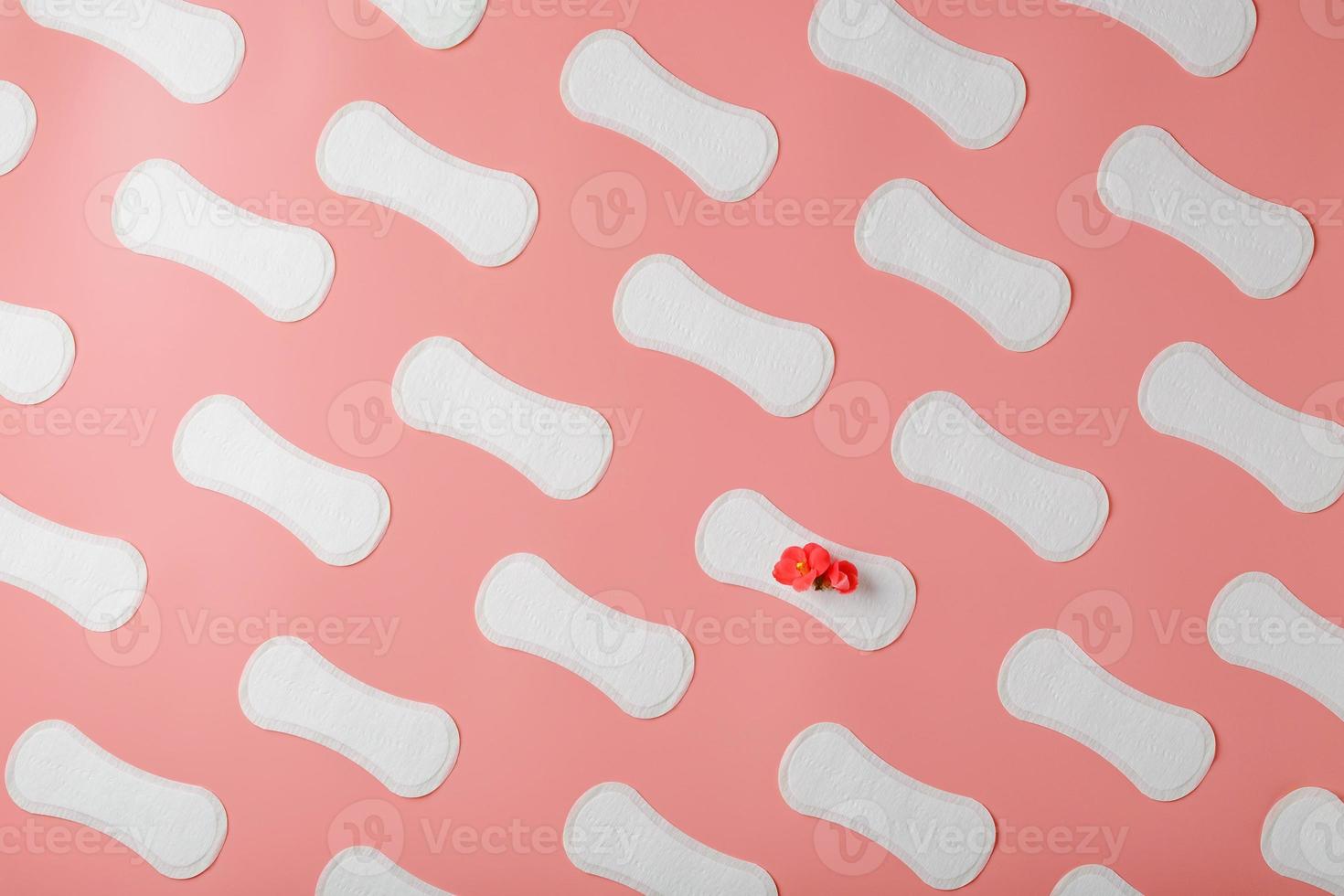 serviettes hygiéniques sur fond rose sous la forme d'un motif diagonal de répétitions, avec une fleur rouge sur le tampon. photo