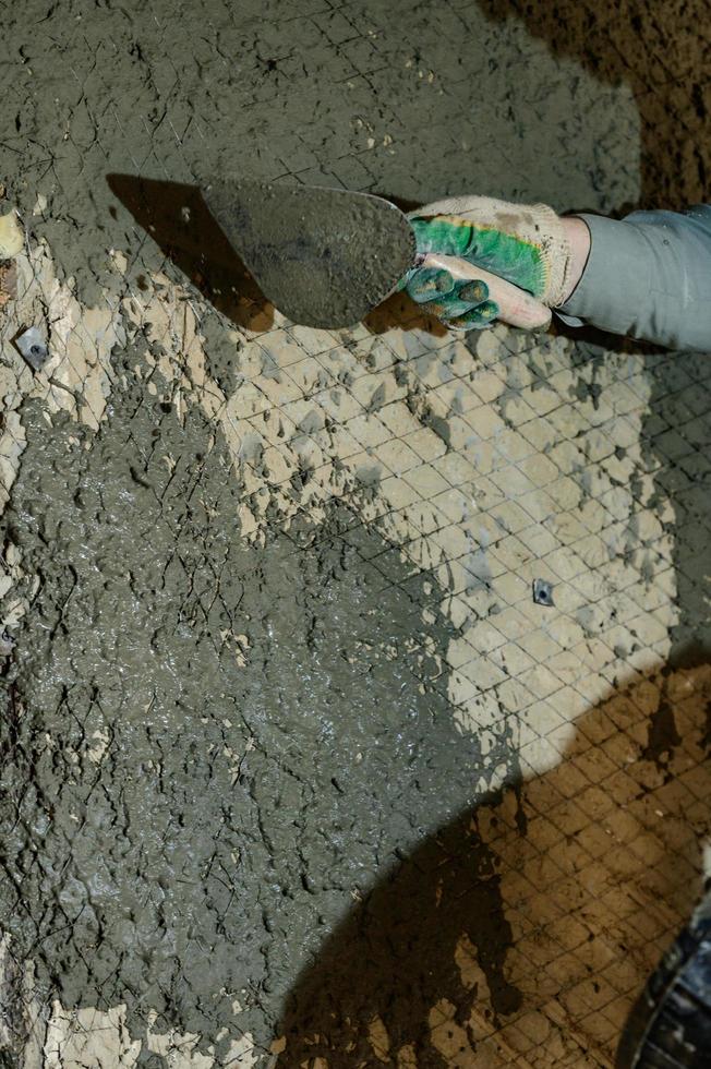 un homme jette du mortier de béton sur le mur, la première couche de plâtre sur le mur, des travaux de réparation en ukraine. photo