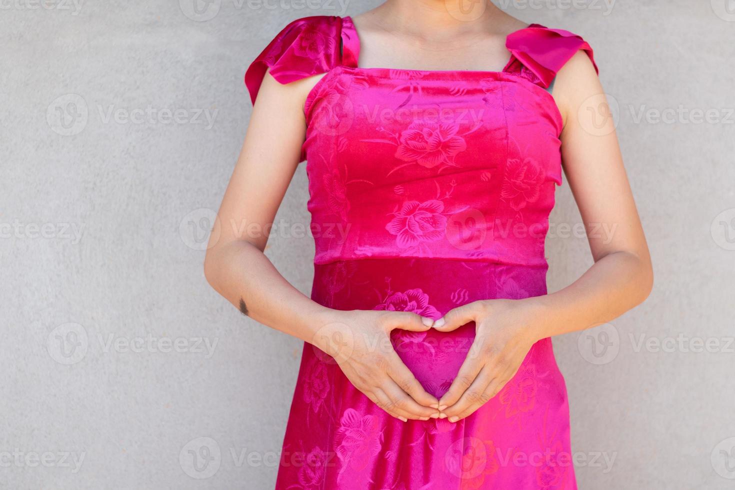 une femme enceinte touche l'estomac avec le symbole de l'amour et l'arrière-plan du mur de ciment, le concept de la mère et du nouveau-né copie l'espace pour le texte et la conception individuels photo