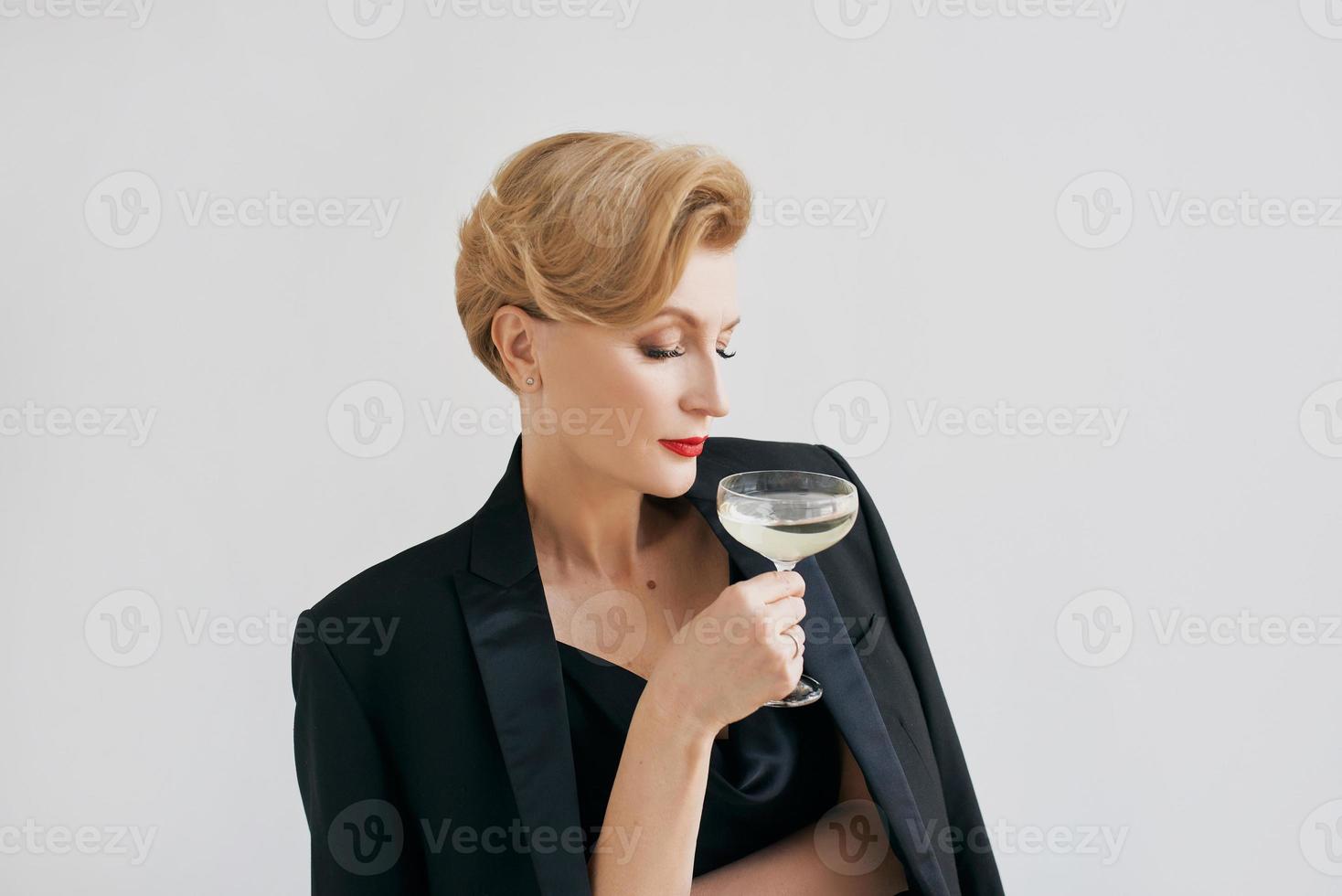 femme élégante et élégante mature en smoking avec un verre de vin mousseux. fête, célébration, concept anti-âge photo