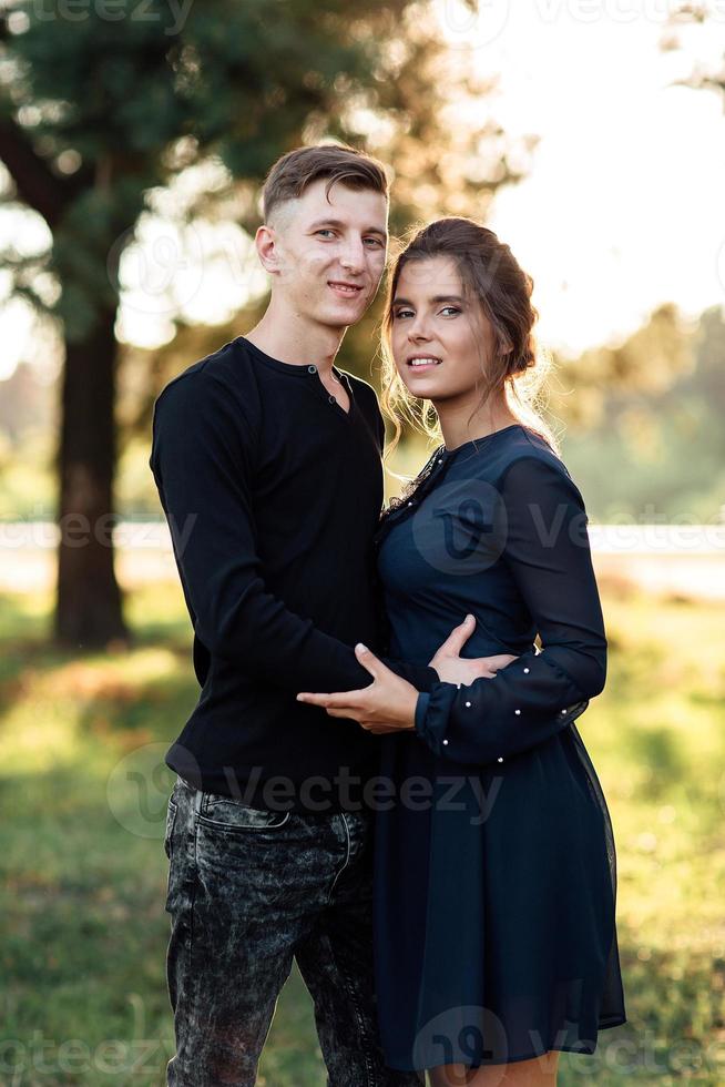 joyeuse jeune femme et homme s'embrassent à l'extérieur dans le parc d'été. couple amoureux ayant rendez-vous et vacances romantiques au coucher du soleil. l'amour et les relations entre les jeunes photo