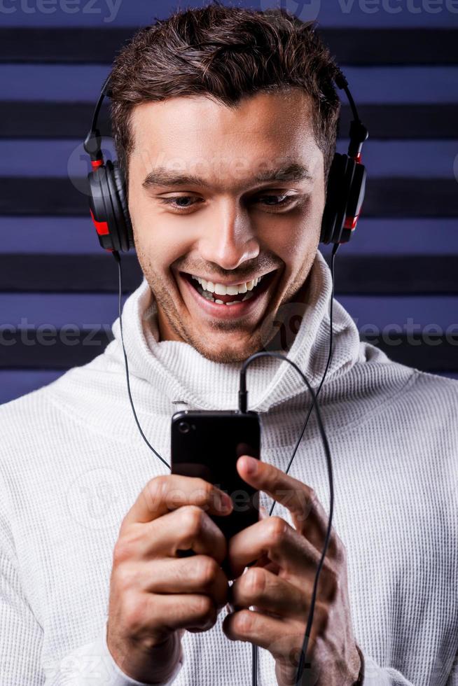 c'est ma chanson préférée beau jeune homme au casque tenant un lecteur mp3 et le regardant avec le sourire tout en se tenant sur un fond rayé photo