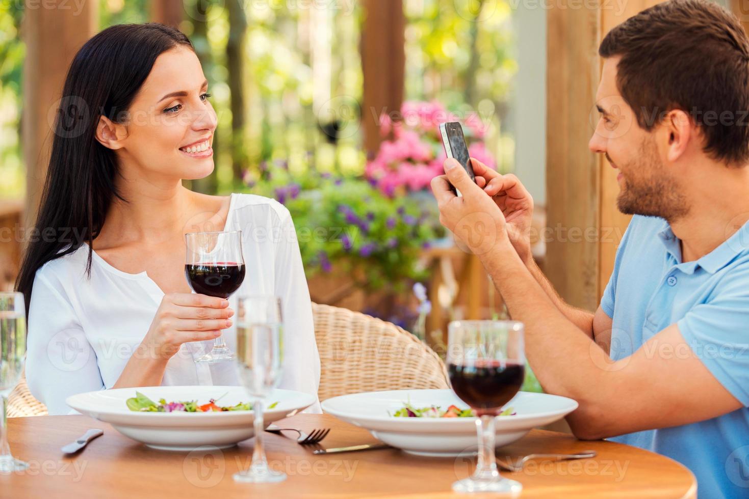 sourire pour la caméra beau jeune homme prenant une photo de sa belle petite amie avec un téléphone intelligent tout en se relaxant dans un restaurant en plein air ensemble