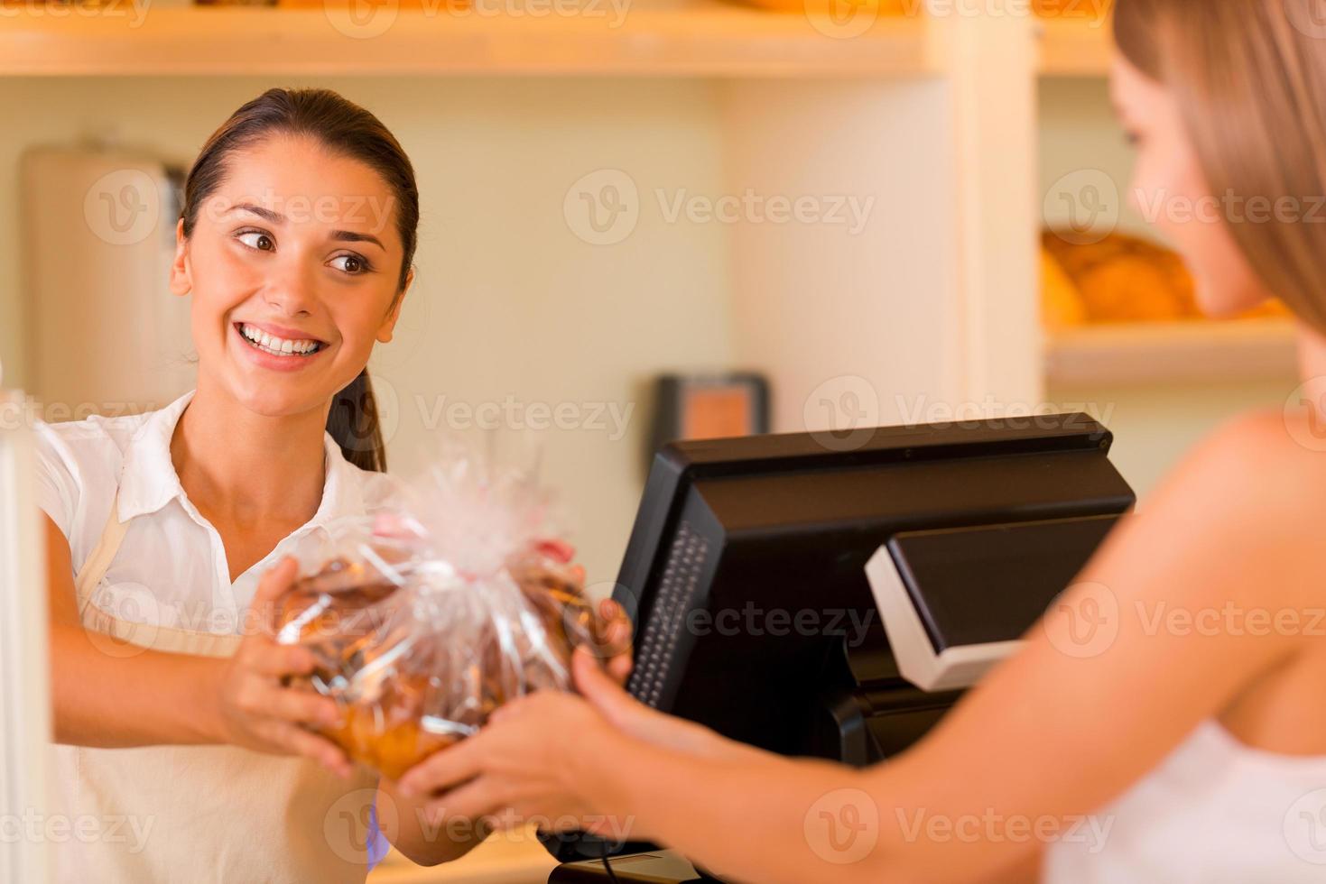 s'il vous plaît profiter de la belle jeune boulangère donnant des biscuits au client et souriant photo