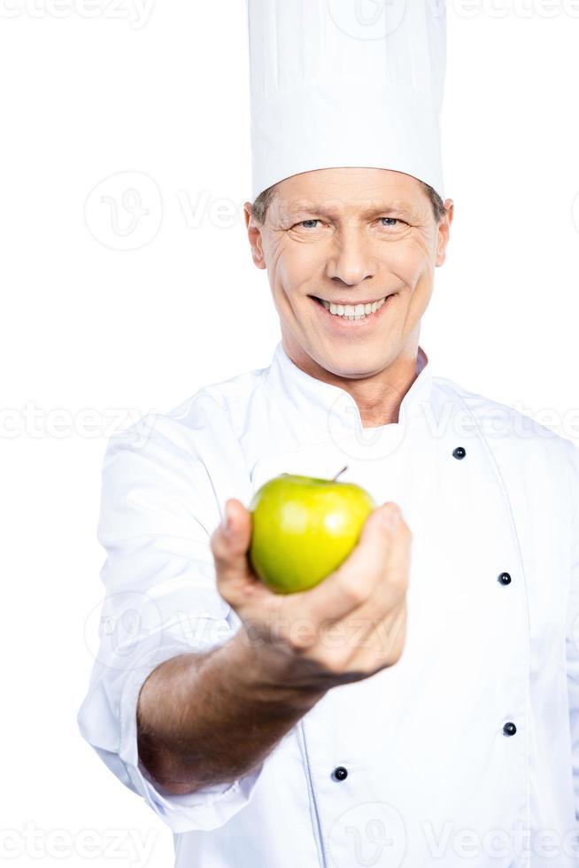 manger sain chef mature confiant en uniforme blanc étirant la pomme verte et souriant en se tenant debout sur fond blanc photo