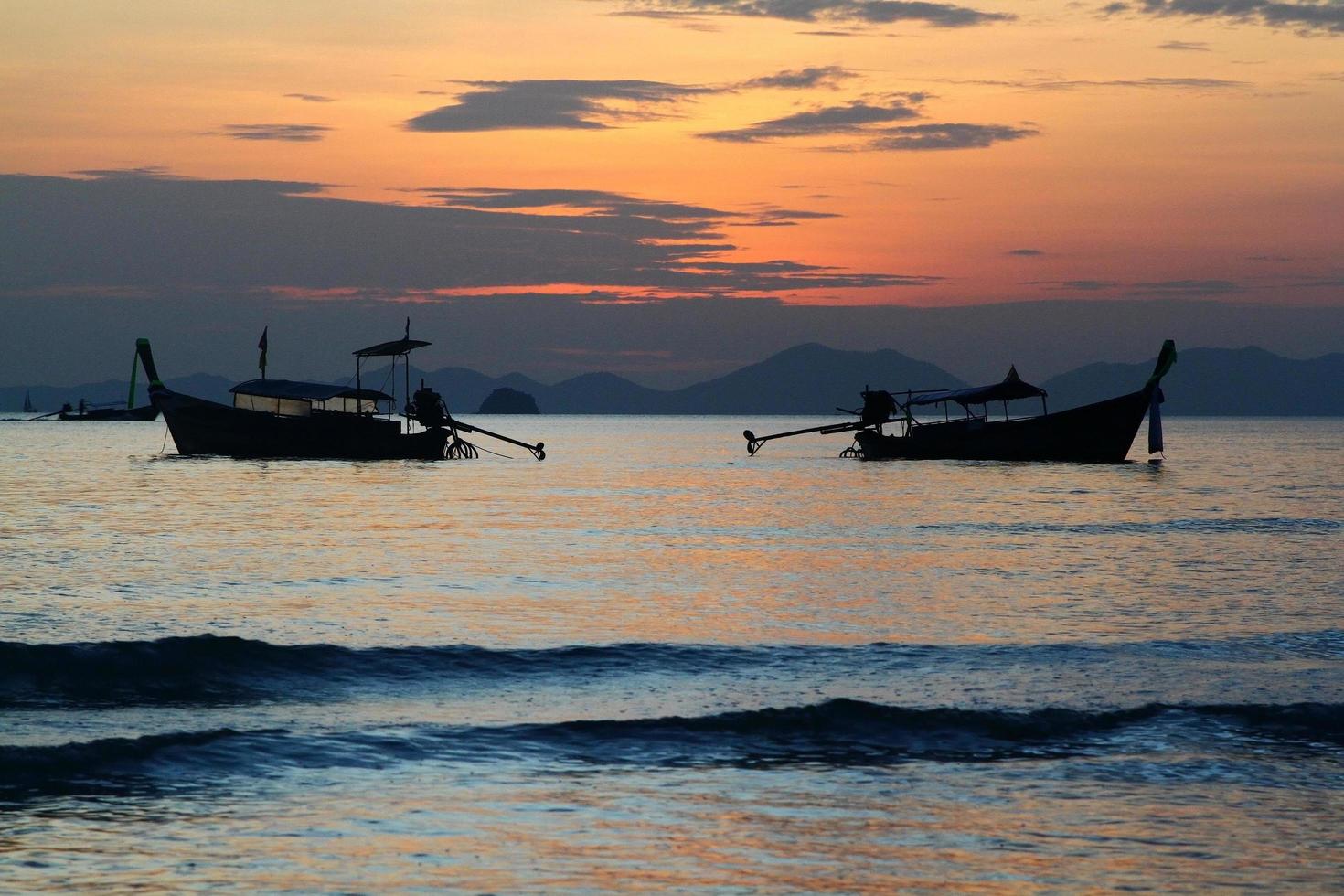 deux silhouettes de bateau longtail sur mer et vague avec ciel orange et fond nuageux à krabi, thaïlande. paysage de l'océan au coucher du soleil. photo
